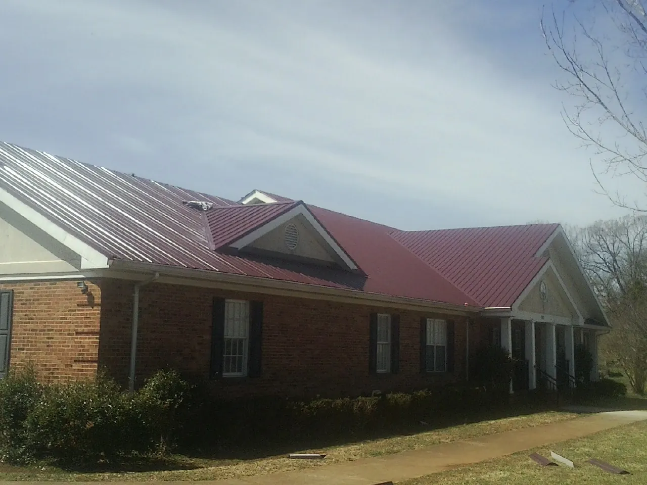 Red metal roof with gabled entries on a long brick building, from a Hail Damage Roof Repair job in Bradford