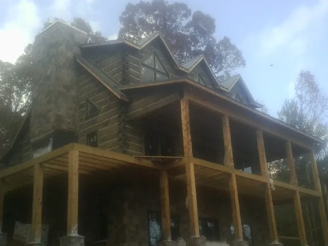 Stone chimney and dormers on a large log home with a timber porch in Bradford